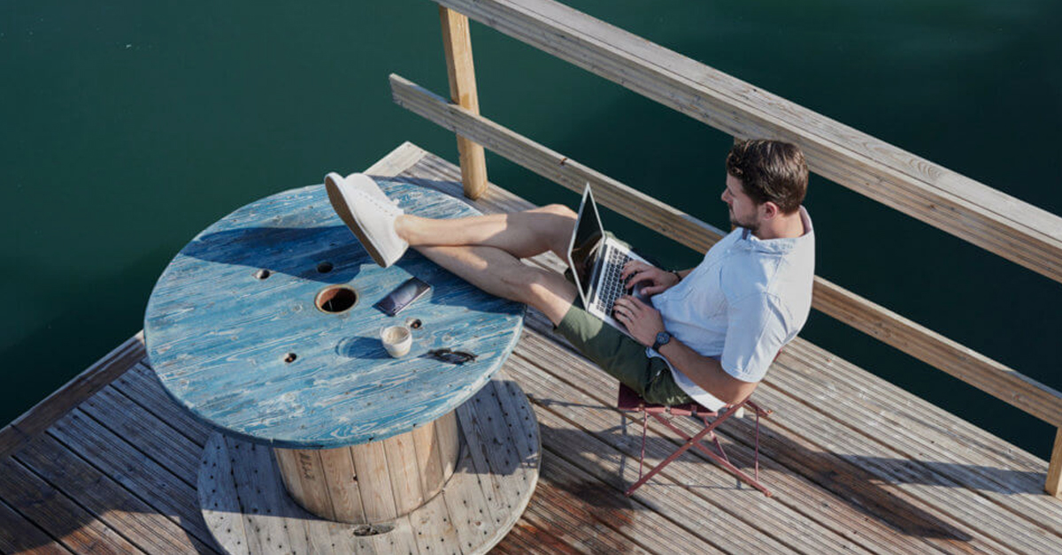 Person sitting on a dock with his laptop on his lap
